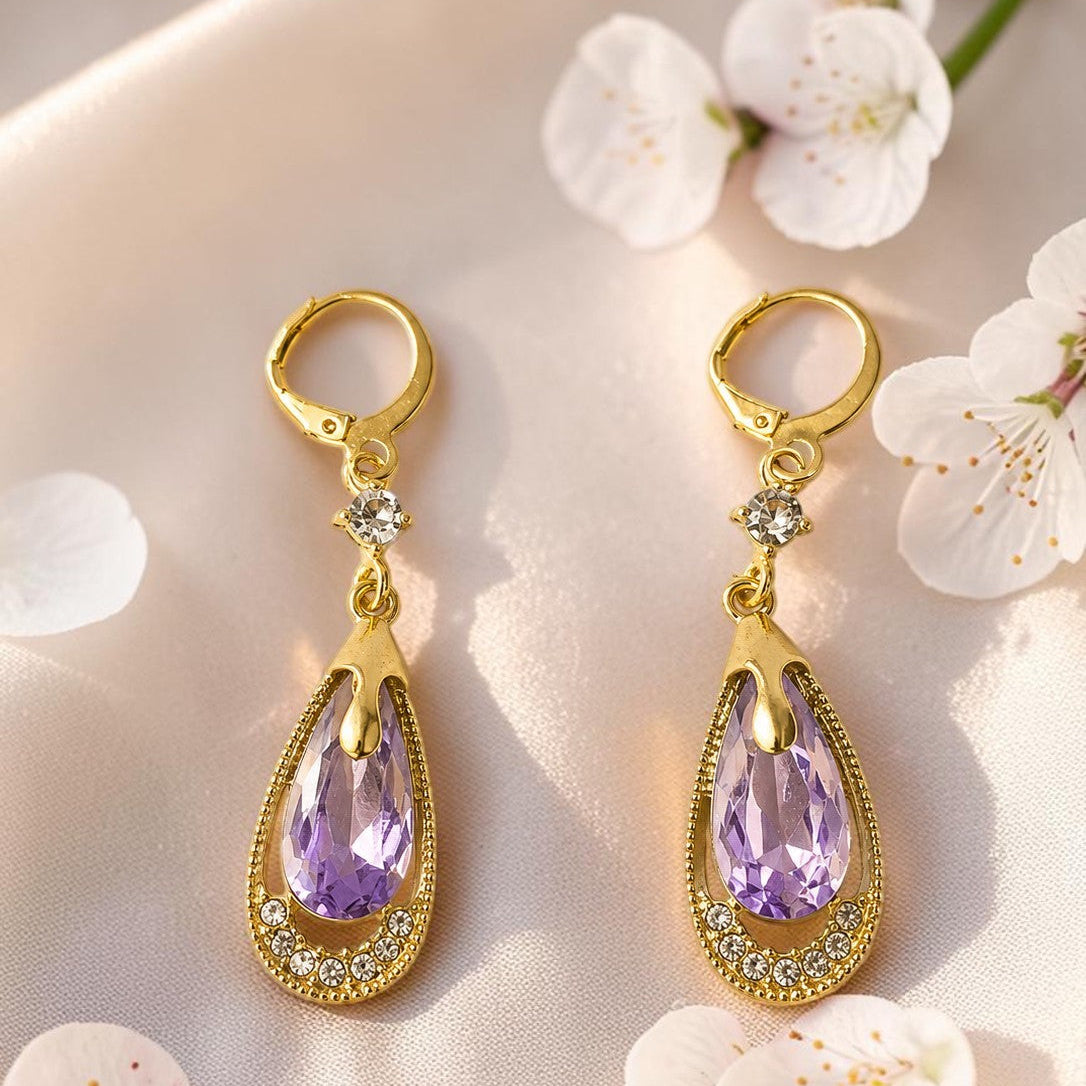 Gold tone  earrings with purple gemstones on a floral background
