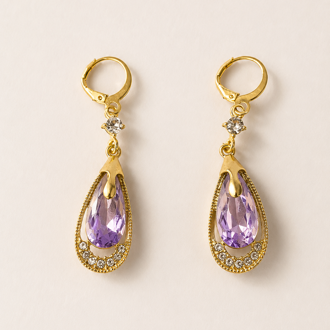 Gold tone earrings with purple teardrop-shaped gemstones on a beige background