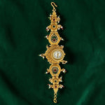 An ornate Victorian-style gold watch chain featuring a central round clock face, intricate filigree details, and small red and white gemstones, displayed on a dark green velvet background.