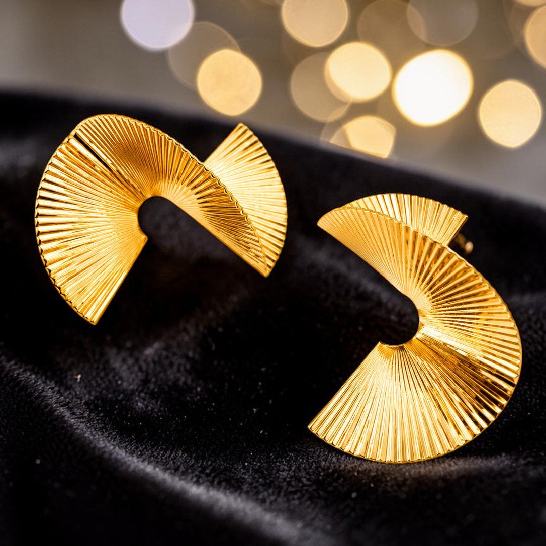 Gold tone earrings on a black background with blurred lights in the background