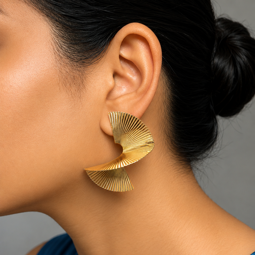 Golden earrings worn by a person with a blue top against a gray background