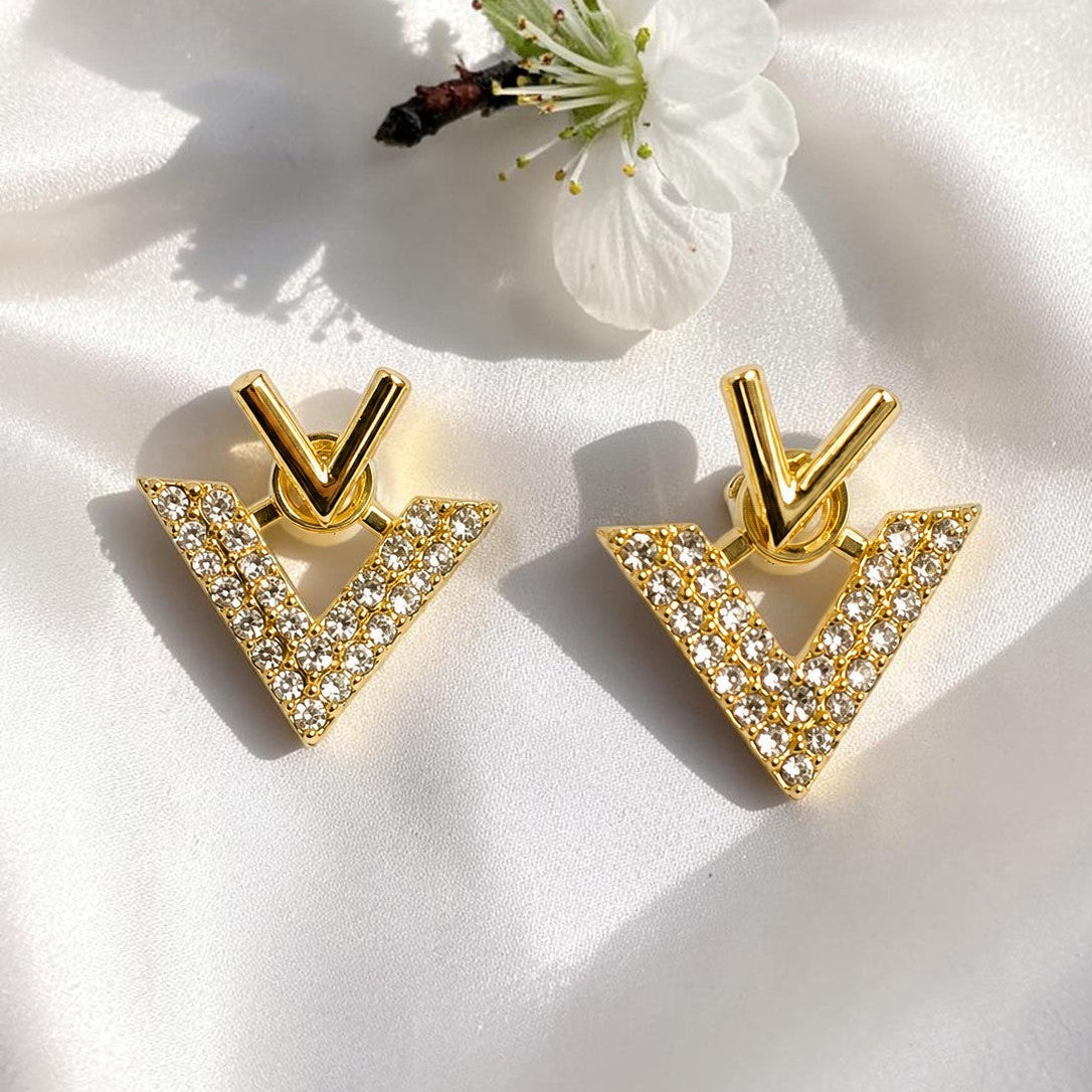 Golden triangle earrings with clear stones on a white surface with a small white flower.