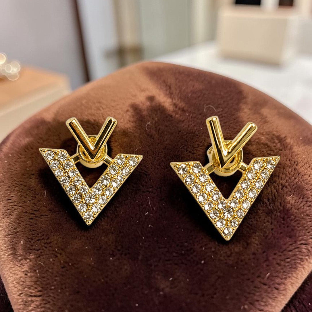 Golden triangle-shaped earrings with clear stones on a brown velvet surface.