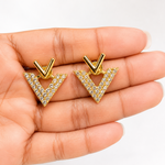 Golden triangle earrings with clear stones held in a hand against a white background