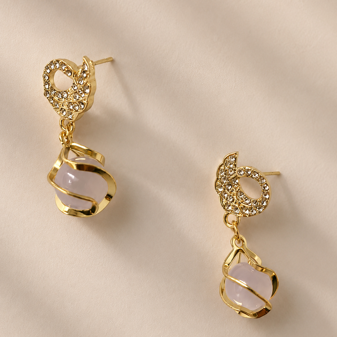 Gold tone earrings with pink stones on a beige background
