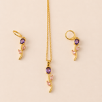 Gold  tone necklace with purple and pink gemstones on a beige background