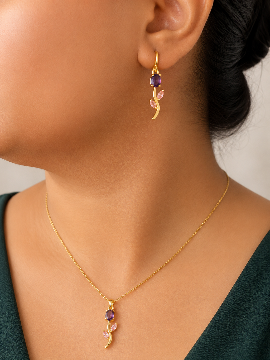 Gold  tone necklace and earrings with purple gemstones worn by a person.