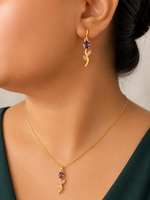 Gold  tone necklace and earrings with purple gemstones worn by a person.