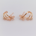 Pair of floral earrings with rose gold and clear gemstone details on a light gray background