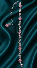A silver-toned chain bracelet featuring pink flower and leaf motifs, displayed on a draped dark teal satin fabric background.