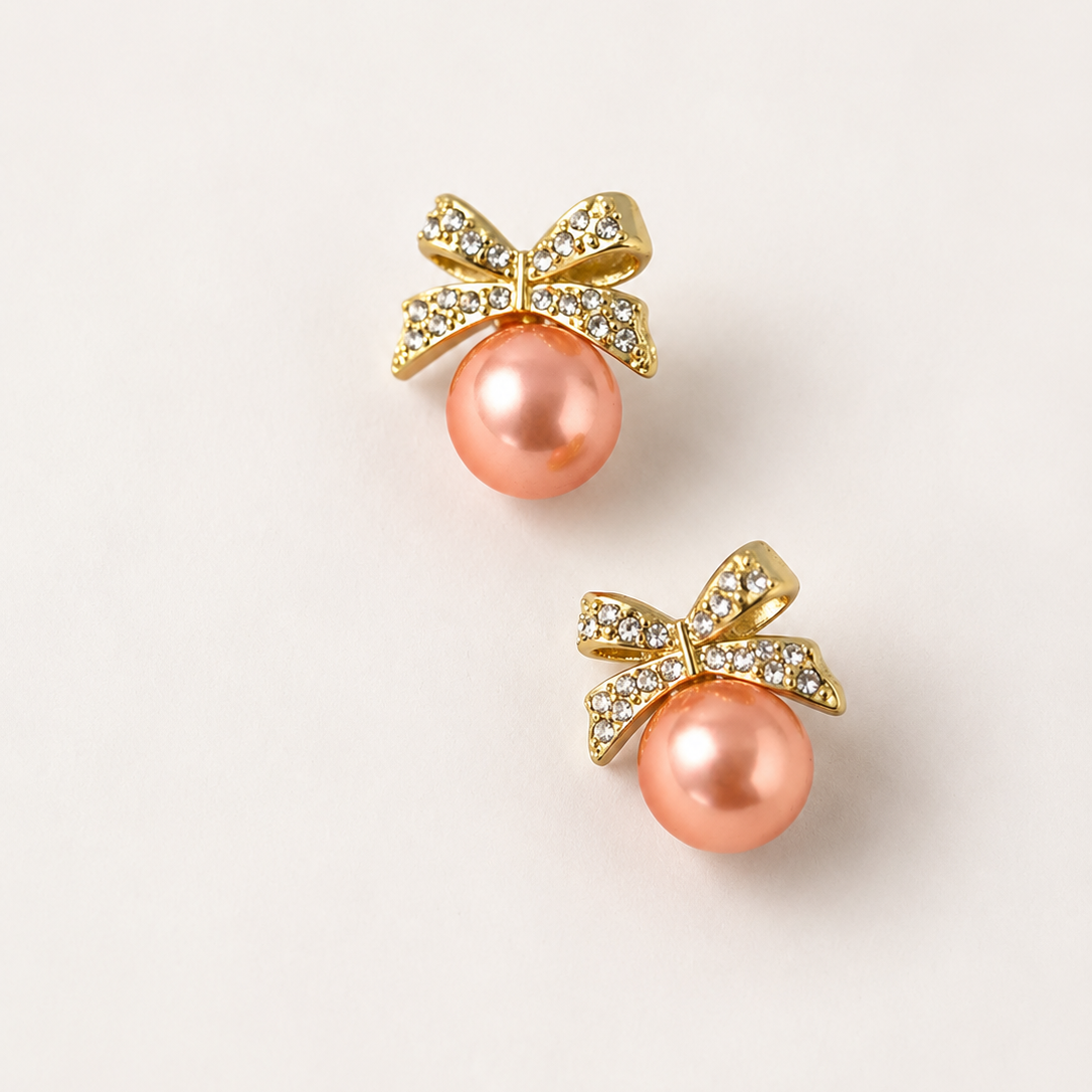 Pair of pink pearl earrings with golden bows on a light beige background