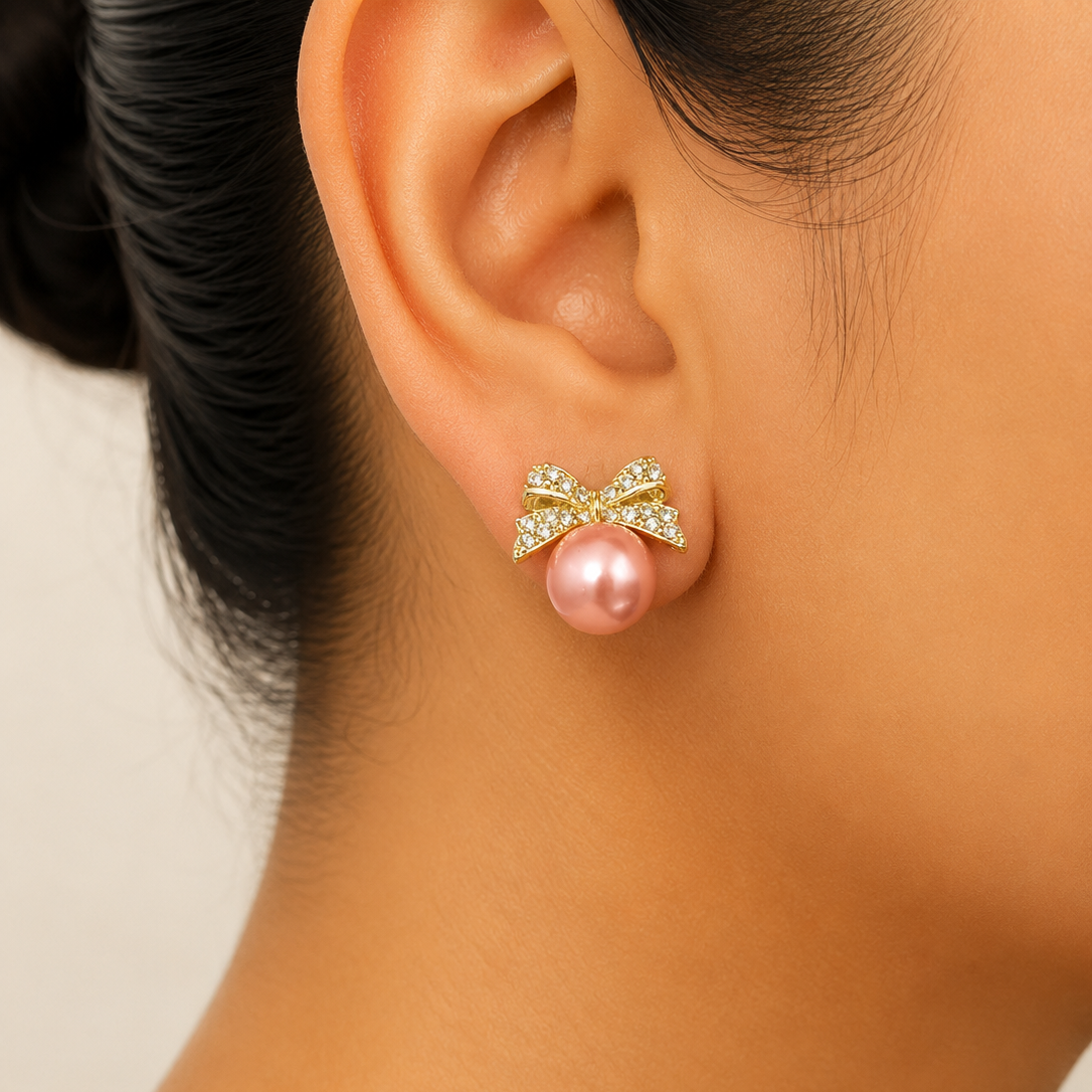 Close-up of an ear wearing a golden bow earring with a pink pearl center.