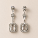 Pair of silver earrings with clear gemstones on a beige background