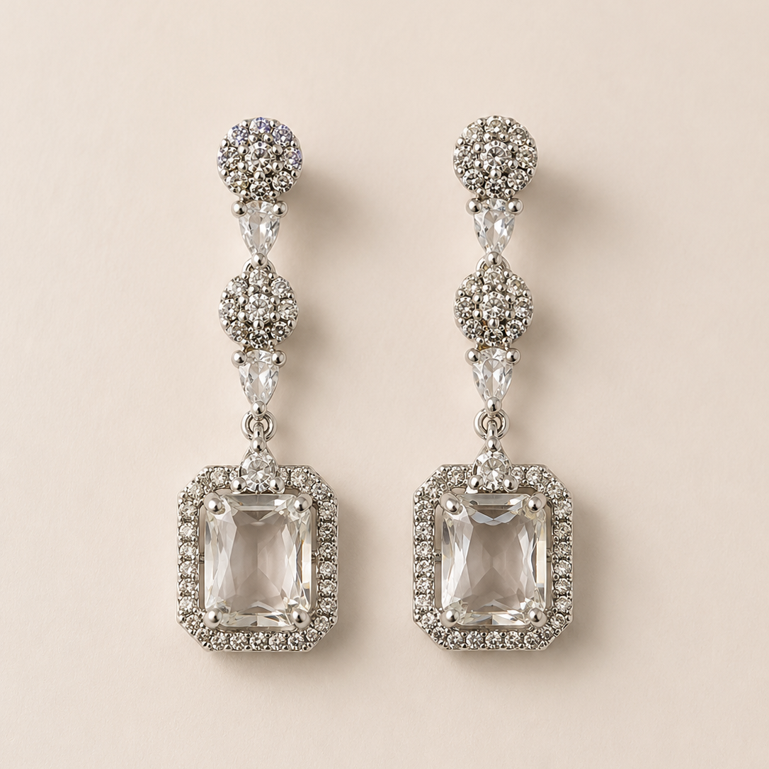 Pair of silver earrings with clear gemstones on a beige background