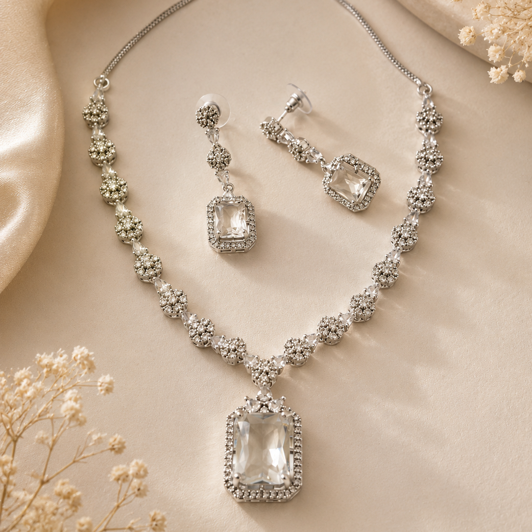 Silver necklace and earrings set on a beige fabric background with dried flowers.