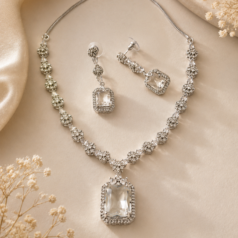 Silver necklace and earrings set on a beige fabric background with dried flowers.