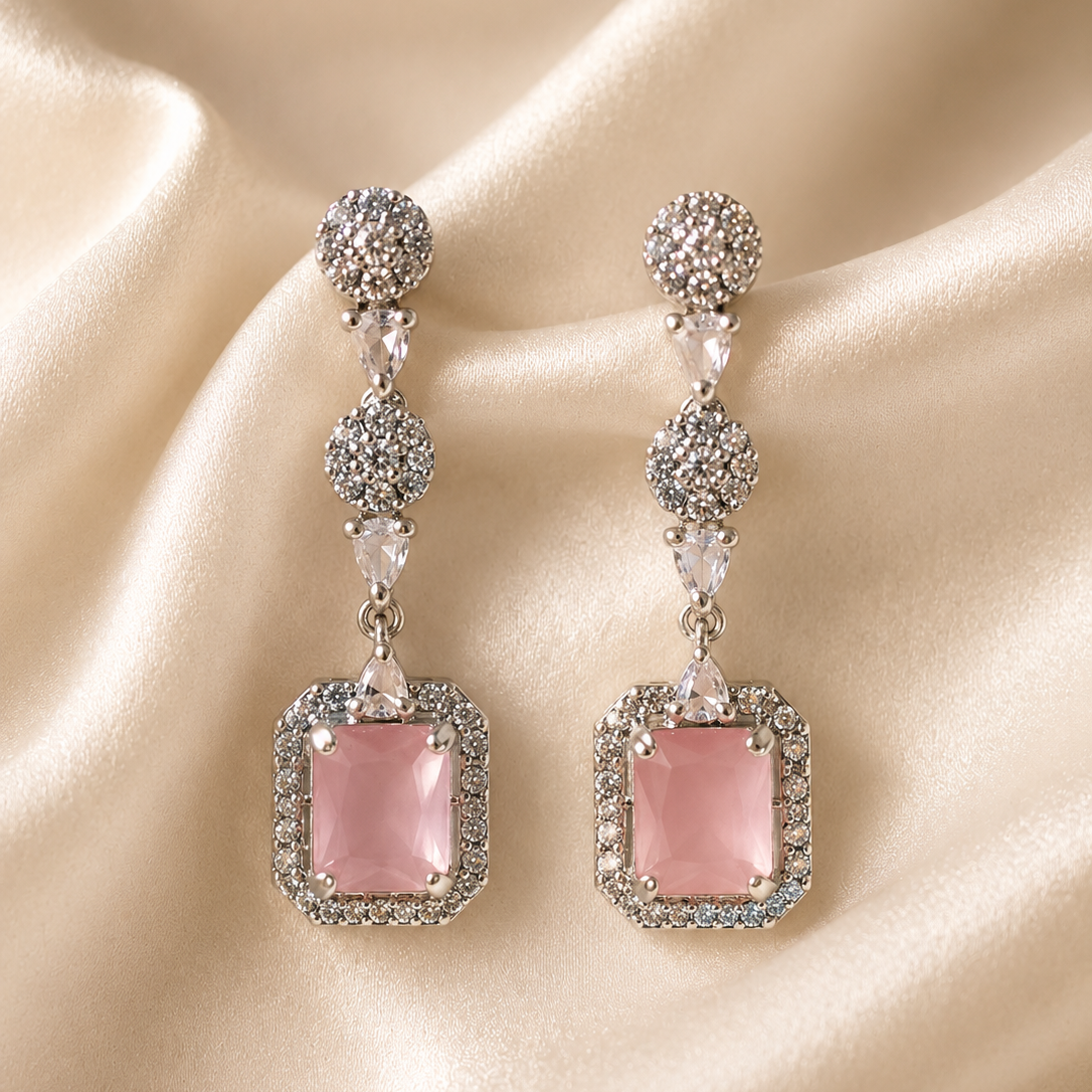 Pink square earrings with silver and crystal details on a beige fabric background