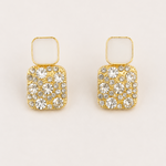 Golden square earrings with crystal embellishments on a beige background