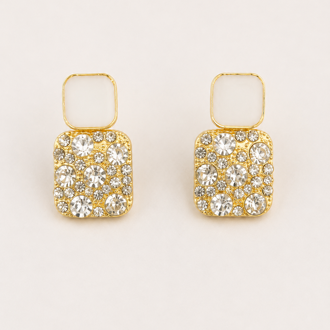 Golden square earrings with crystal embellishments on a beige background
