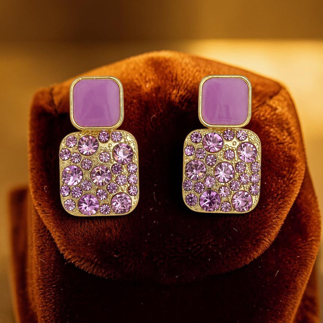 Pair of square-shaped earrings with purple stones on a brown velvet surface.