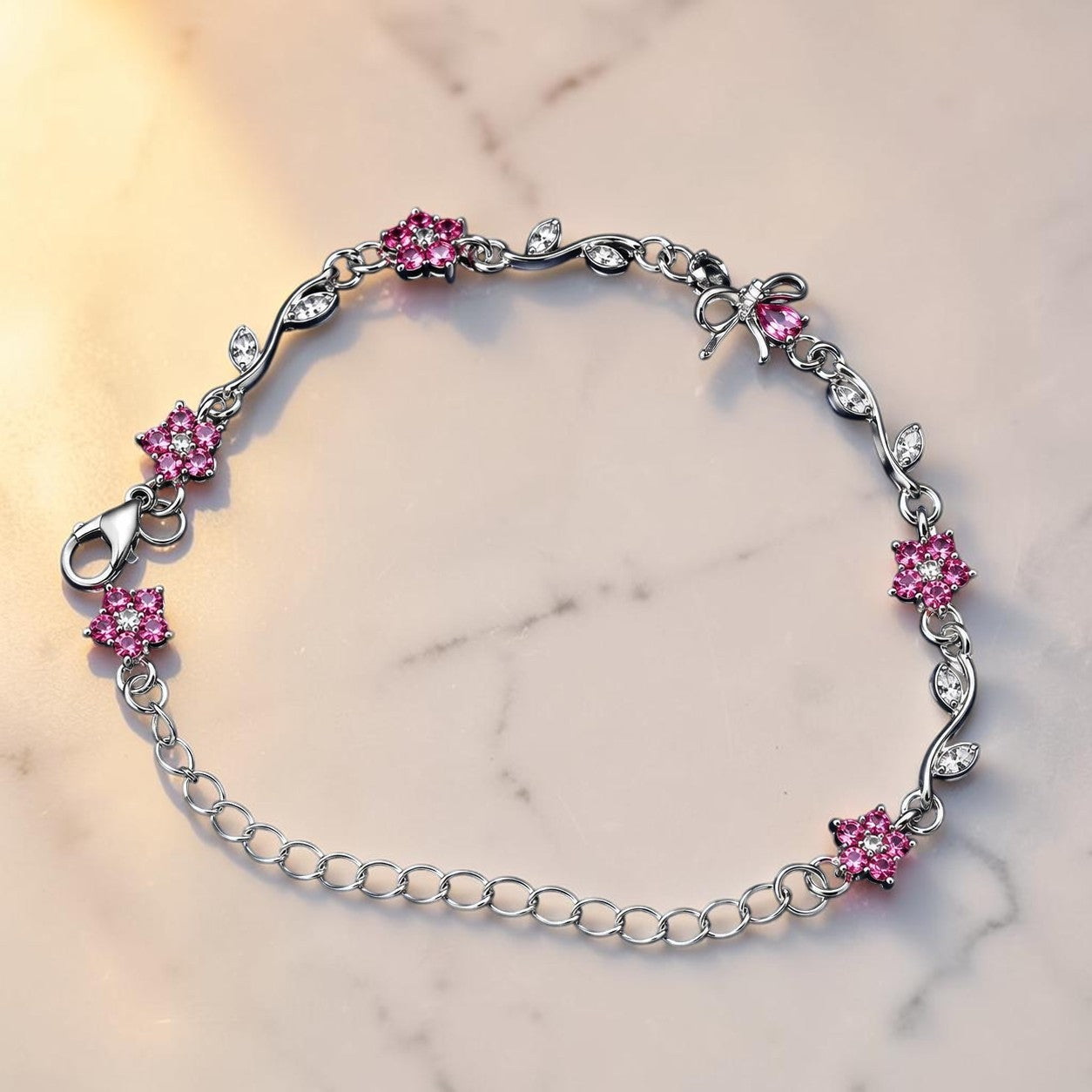 A silver chain bracelet with pink crystal starburst flower charms and clear crystal leaf accents, displayed on a light marble surface.