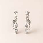 Pair of silver earrings with leaf and crystal designs on a beige background