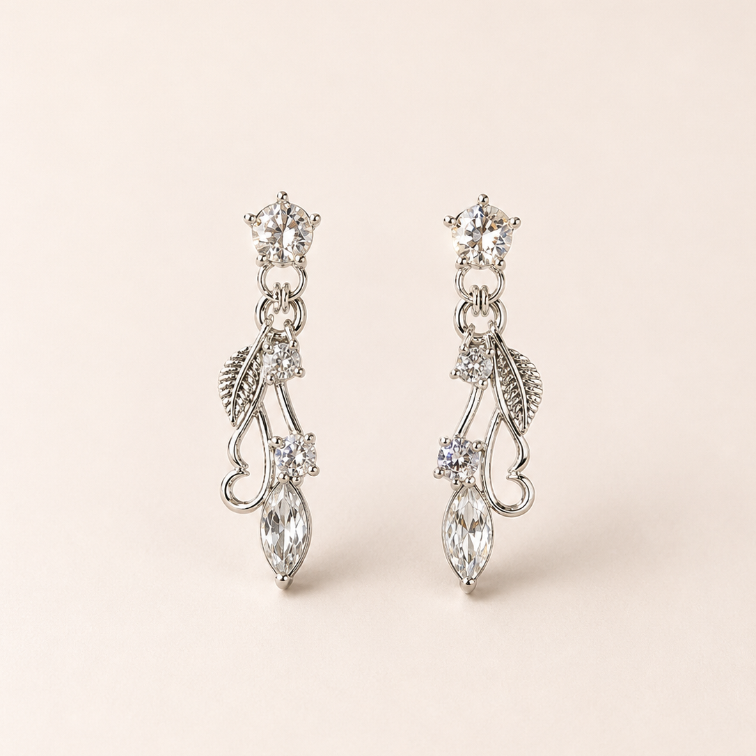 Pair of silver earrings with leaf and crystal designs on a beige background