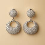 Pair of silver tone earrings with round top and circular bottom on beige background