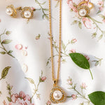 Gold tone necklace with a pearl pendant and matching earrings on a floral background