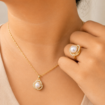 Gold tone necklace and ring with pearl accents on a neutral background