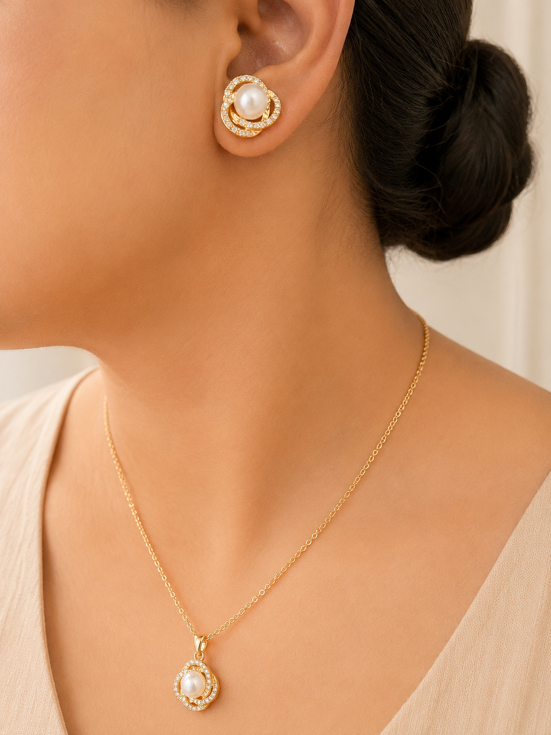Gold tone necklace and earrings with pearl accents worn by a person.