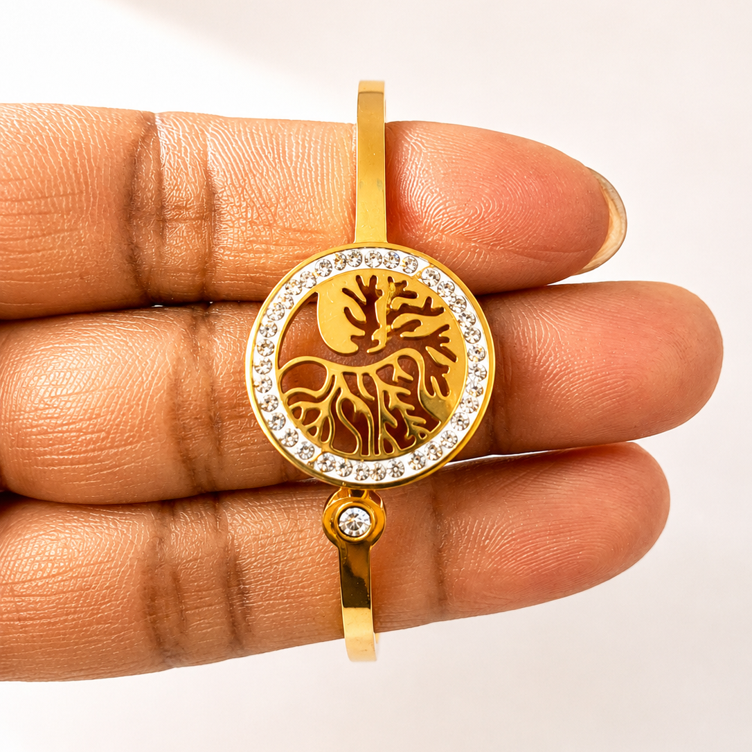 Gold tone pendant with tree design held between fingers on a white background