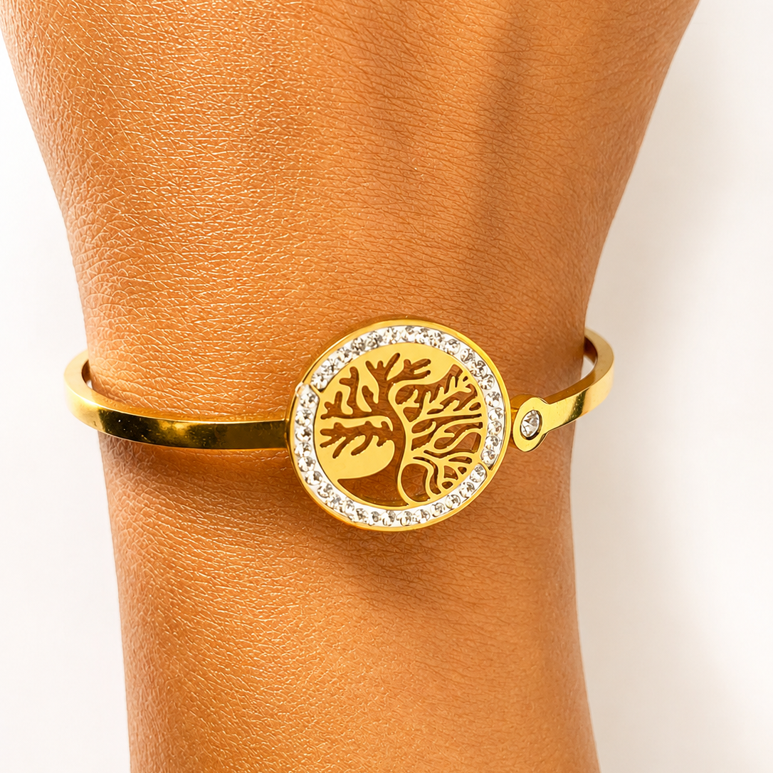 Gold tone bracelet with a tree of life design on a wrist against a neutral background