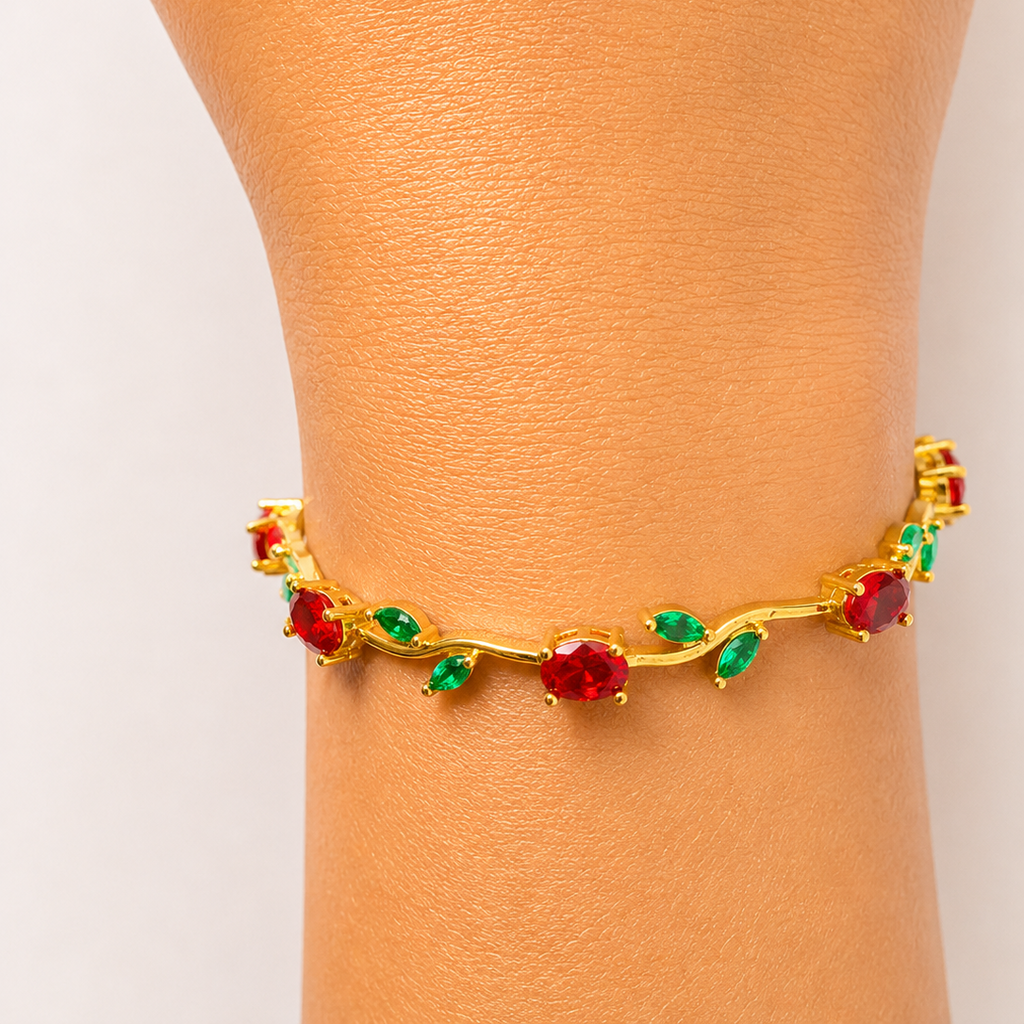 Gold tone bracelet with red and green gemstones on a wrist against a light background