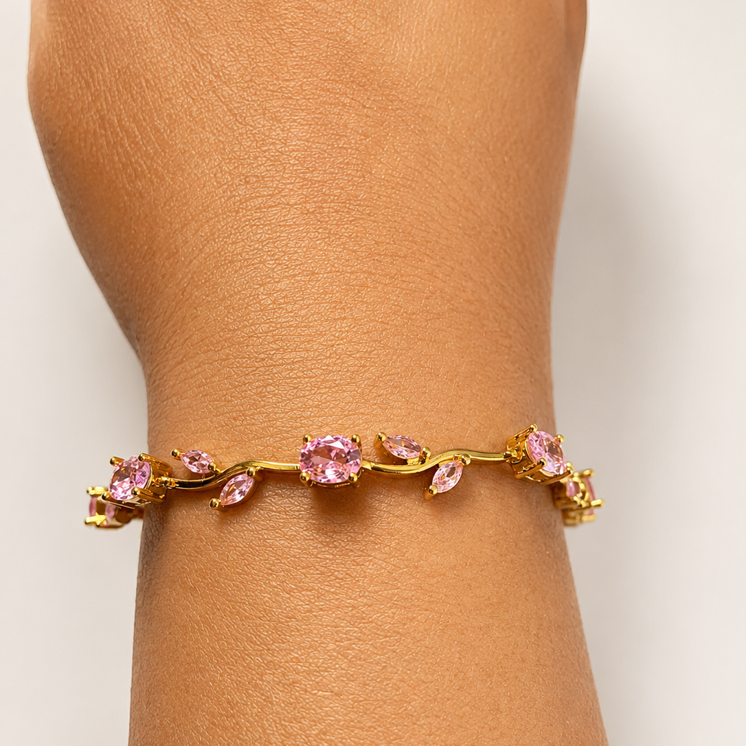 Gold tone bracelet with pink gemstones on a wrist against a light background