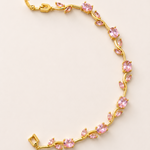 Gold tone bracelet with pink gemstones on a light beige background