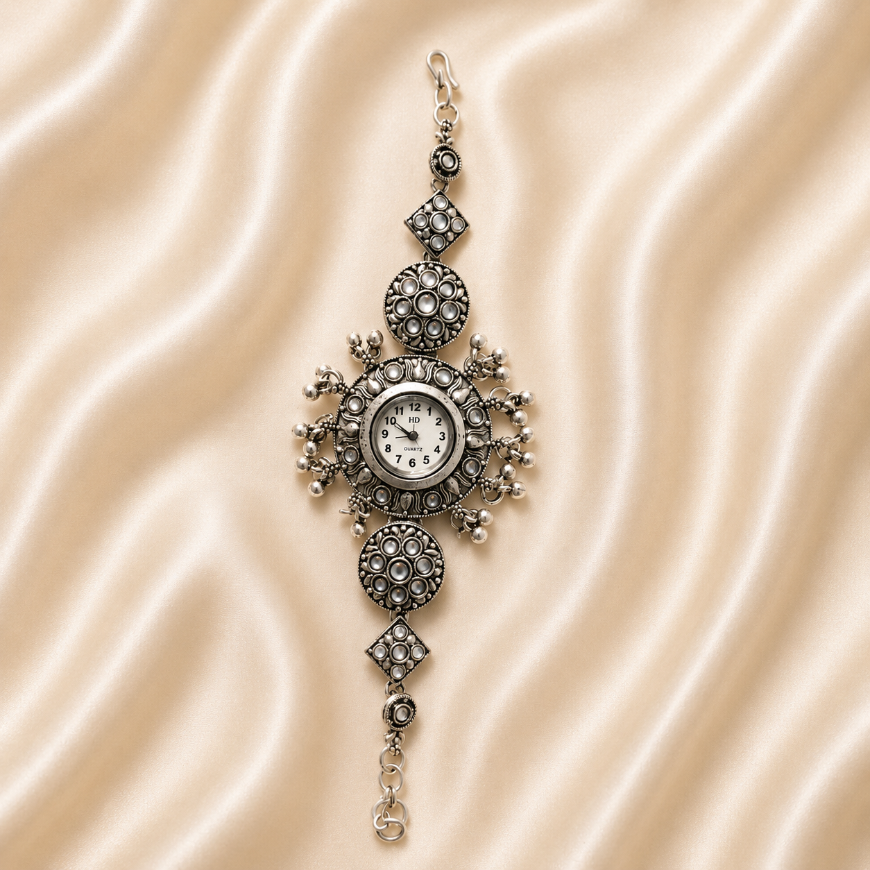 An ornate vintage-style silver-toned pendant watch with a circular dial, set against a draped beige satin fabric background.