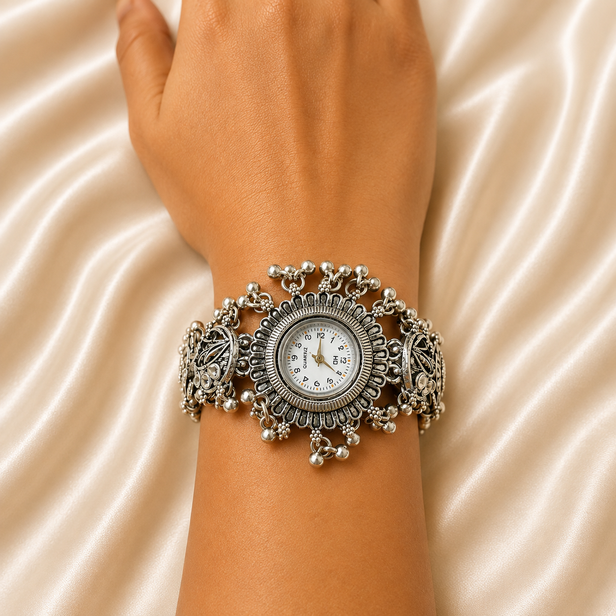 A close-up of a person's wrist wearing an ornate silver-toned wide bracelet watch with a round white dial, set against a draped satin fabric background.