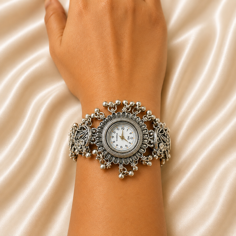 A close-up of a person's wrist wearing an ornate silver-toned wide bracelet watch with a round white dial, set against a draped satin fabric background.