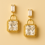 Gold tone earrings with clear gemstones on a beige background