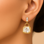 Gold tone earring with a clear gemstone on a mannequin ear against a beige background