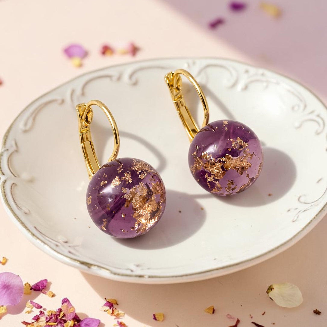 Purple earrings with gold accents on a decorative plate with scattered flowers.