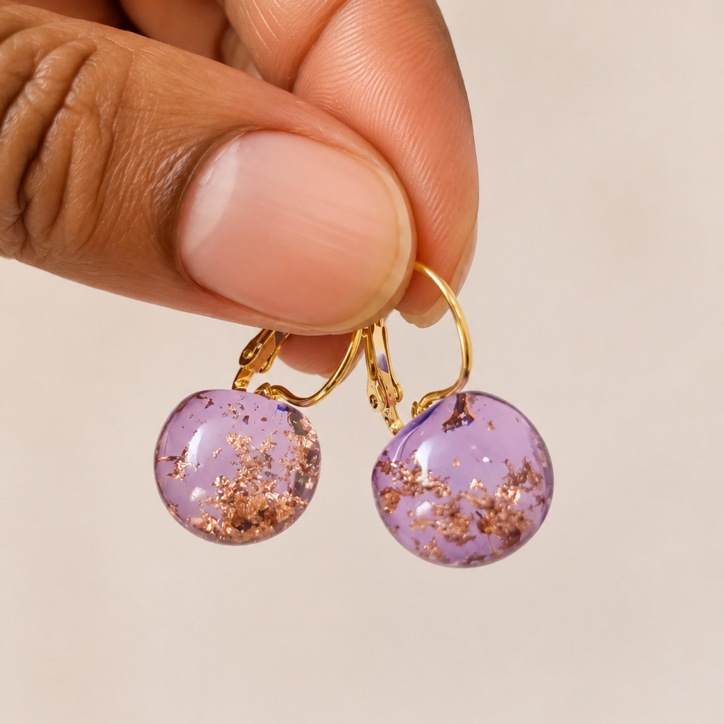 Purple earrings with gold accents held by a hand against a beige background