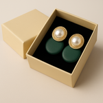 Pair of earrings with gold tone and pearl design in a beige box on a beige background