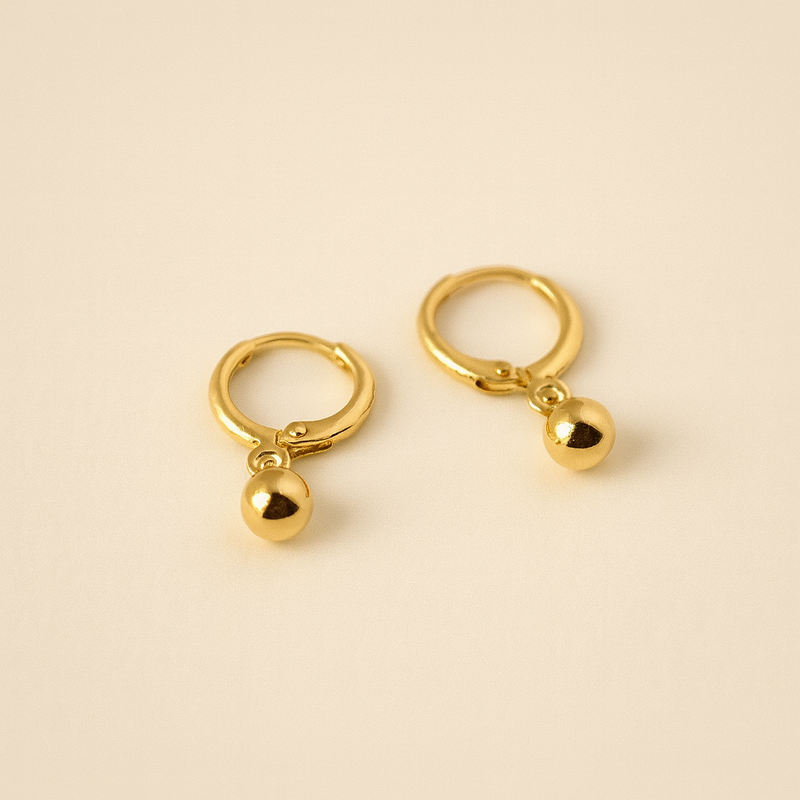 Pair of gold hoop earrings with small spherical charms on a beige background