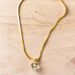 Gold tone necklace with a heart-shaped pendant on a light wooden surface