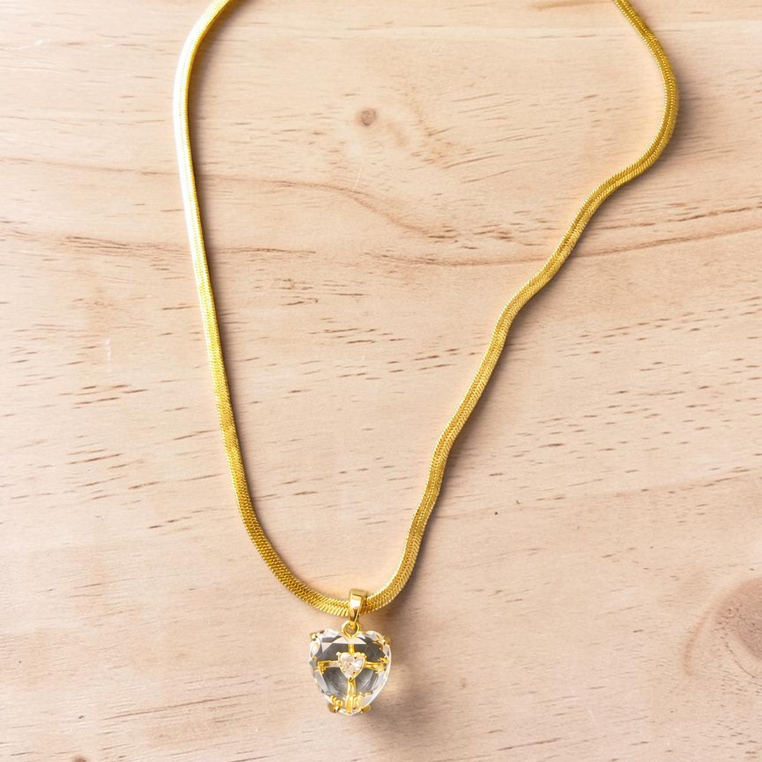 Gold tone necklace with a heart-shaped pendant on a light wooden surface