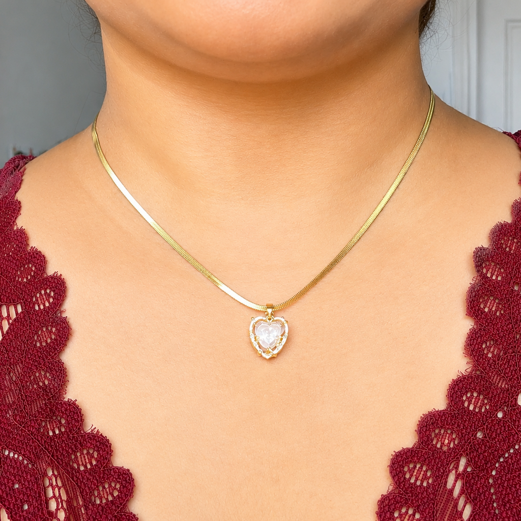 Gold tone necklace with a heart-shaped pendant worn by a person in a red lace garment.