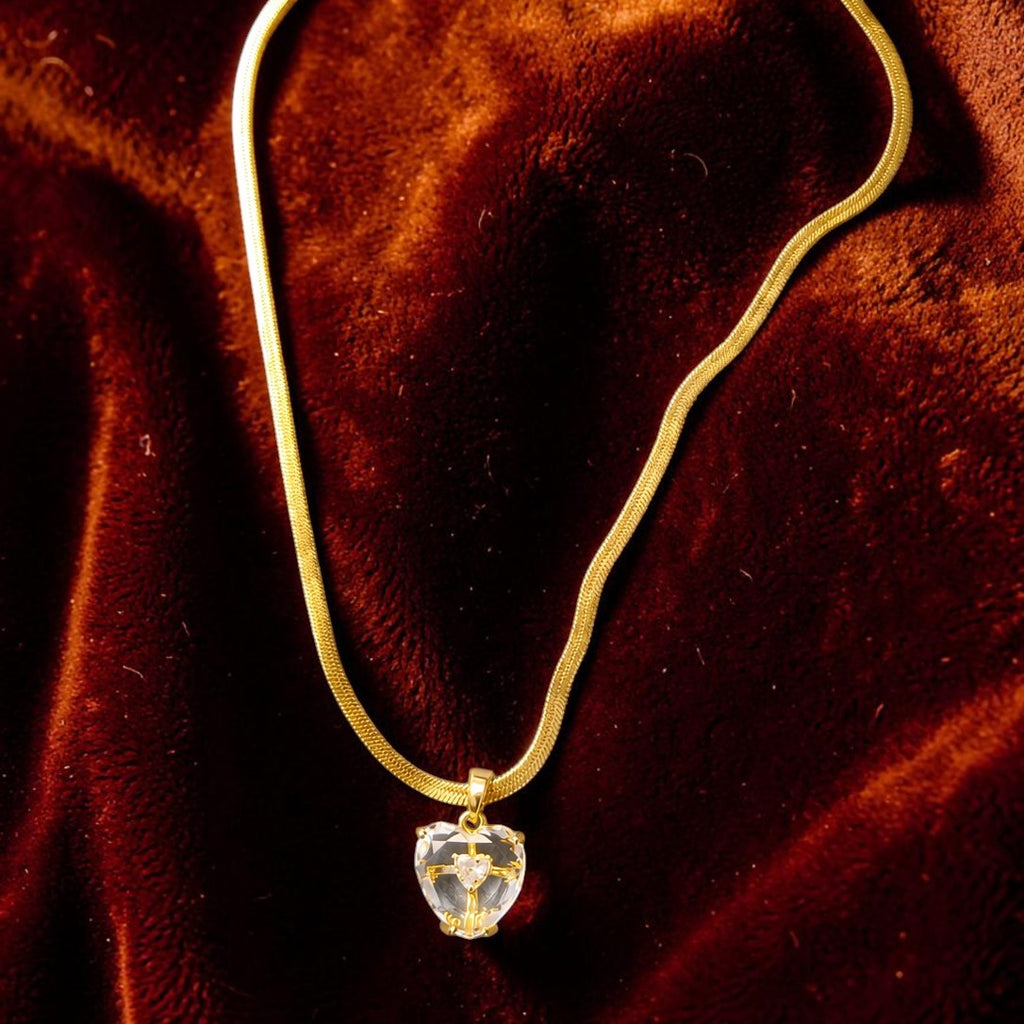 Gold tone necklace with a heart-shaped pendant on a red velvet background