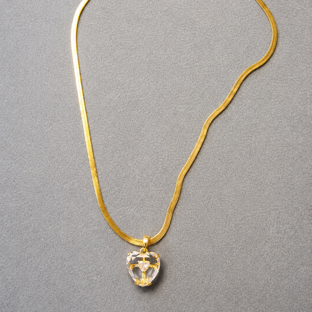 Gold tone necklace with a clear crystal pendant on a gray background